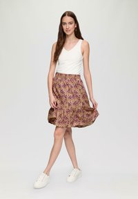 Blumiger Rock mit lila und gelben Mustern, ausgestelltem Design und elastischem Bund; kombiniert mit einem weißen Tanktop und weißen Sneakers.