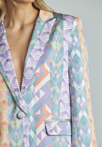 Blazer colorido con patrones geométricos en tonos pastel, con cuello de muesca, cierre de un solo botón y detalle de bolsillo.