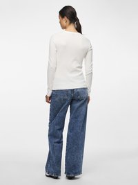 Valkoinen pitkähihainen paita, jossa on ribbineulospinta, yhdistetty korkeavyötäröisiin leveälahkeisiin sinisiin farkkuihin, joissa on haalistettu pinta ja ommellut takataskut.