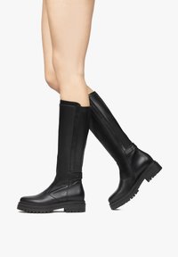 Bottes noires en cuir jusqu'au genou avec une finition lisse, semelle robuste et fermeture éclair sur le côté. Présentent une cheville étroite et un tige large avec des accents minimaux.