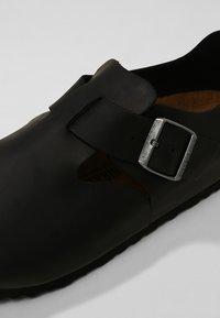 Fekete gumiszandál, nyitott dizájnnal, ezüst fémcsattal és textúr�ált talppal, a belsejében látható parafa talppal.