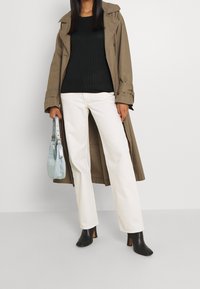 Hnědý trench coat, černý žebrovaný svetr, bílé rovné džíny a černé kotníčkové boty na podpatku. Drží světle modrou kabelku.