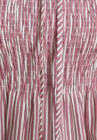 Gros plan d’un tissu à rayures verticales roses, blanches et noires avec des détails smockés froncés et des coutures texturées.