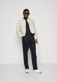 Lett quiltet bomberjakke, mørk turtleneck, løse marineblå bukser og hvite sneakers med brune detaljer. Tilbehøret inkluderer liten hvit veske og solbriller.
