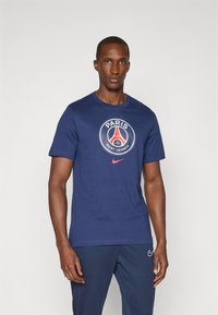 Marineblå bomulds t-shirt med rund halsudsk�æring, korte ærmer og et rundt Paris Saint-Germain-logo i rød og hvid på fronten.