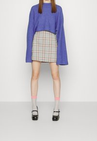 Pull violet raccourci, jupe à carreaux beige et noir, chaussettes bleu clair à motif quadrillé avec bordures roses, et chaussures Mary Jane noires.