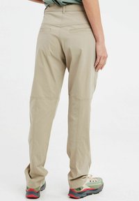 Šviesiai rudos kelnės su tiesiais kojų kirpimais, pagamintos iš lengvos medžiagos. Yra dvi užpakalinės kišenės ir šiek tiek siuvimo detalių ant siūlių.