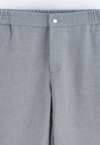 Pantalon gris à texture lisse, ceinture élastique et fermeture par bouton métallique. Présente un design simple sans motifs ni accents visibles.