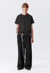 T-shirt nera oversize abbinata a pantaloni larghi neri con coulisse bianca. L'outfit ha un taglio casual e rilassato.