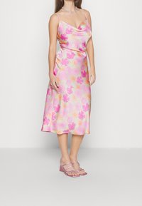 Robe midi florale rose pastel avec encolure bénitier, bretelles spaghetti et motif floral multicolore. Associée à des sandales à talons roses clairs.