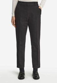 Svarta rakbenade byxor i bomull, med platt fram, sidofickor och bälteshällor, kombinerat med svarta loafers och strumpor.