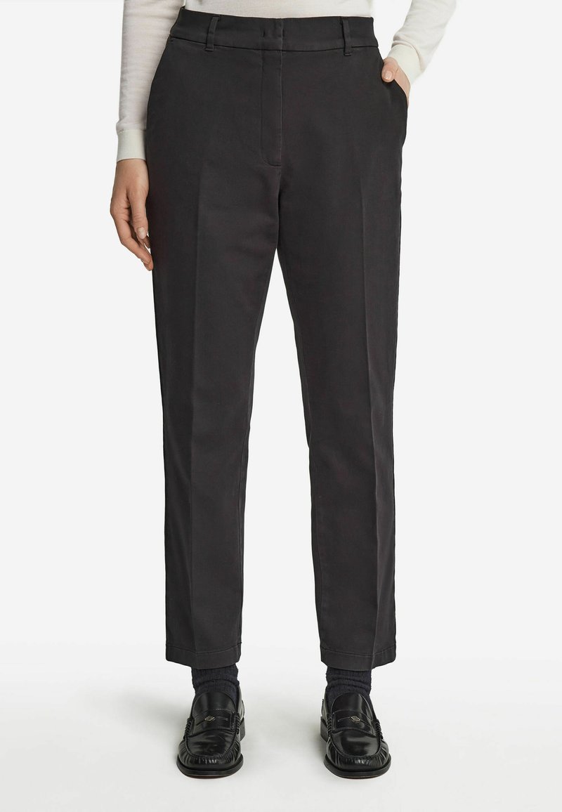 Svarta rakbenade byxor i bomull, med platt fram, sidofickor och bälteshällor, kombinerat med svarta loafers och strumpor.