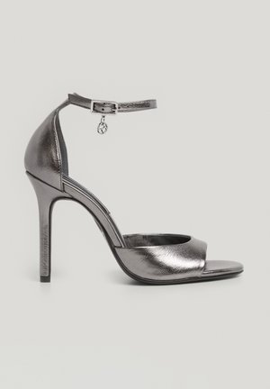 Metaalachtig zilveren hoge hak sandalen met een brede enkele voorkantstrap, enkelband met gesp en een slanke naaldhak. Gladde textuur.