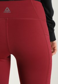 Bordowe legginsy wykonane z elastycznego materiału. Posiadają detale szwów oraz logo Reebok na pasku. Gładka tekstura i dopasowany krój.
