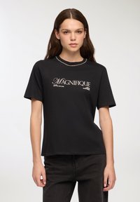Czarna bawełniana koszulka z krótkim rękawem, z białym nadrukiem "MAGNIFIQUE" i luźnym krojem. Gładka tekstura, okrągły dekolt.