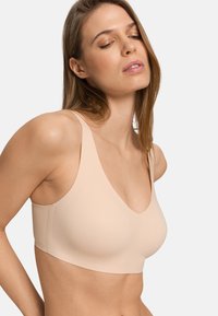 Ljust beige bh med djup V-ringning, breda axelband och slät textur. Enkel design utan synliga sömmar eller metall detaljer.