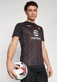 Čierny športový dres s červenými vertikálnymi pruhmi, s centrálnym logom a textom "FUTBAL!" Model drží čierno-biely futbal.