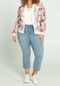 Cárdigan floral translúcido en rosa y malva, con ribetes blancos, combinado con una blusa blanca y jeans cortos de color azul claro. Zapatillas blancas con acentos verdes.