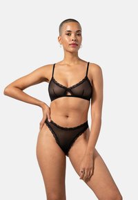 Musta alusvaatesetti, joka sisältää läpikuultavan bralette-pitsin reunuksella ja samanlaiseen pitsiin yhdistelevät stringit, jotka esittelevät herkän ja modernin muotoilun.