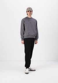 Grå sweatshirt med rund hals og diskret branding, parret med sorte sweatpants og grå sneakers med hvide snørebånd og accenter.
