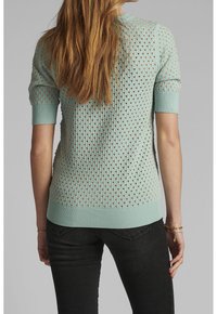 Pull vert menthe à manches courtes avec un design texturé en maille ouverte et des poignets et ourlet côtelés. Porté avec un jean foncé, vue de dos.