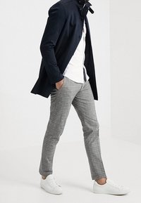 Námořnická bunda s knoflíkovým zapínáním, bílá košile, šedé kostkované kalhoty a bílé tenisky. Slim fit s čistým, moderním siluetou.