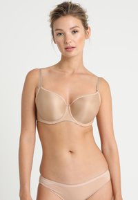 Reggiseno strutturato color beige chiaro con coppe in schiuma liscia, spalline regolabili e supporto con ferretto. Design semplice, senza motivi visibili o accenti.