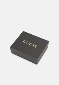 Musta ristkülikukujuline karp sileda tekstuuriga ja kuldse "GUESS" logoga peal. Suletud tasase kaanega, ilma nähtavate musterite või riistvarata.