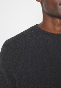 Schwarzer strukturierter Pullover mit Rundhalsausschnitt und geripptem Saum, aus einem weichen, flauschigen Material und in einer taillierten Silhouette.