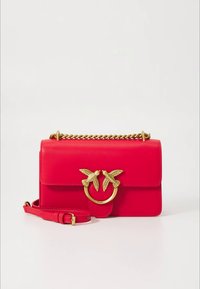 Κόκκινη δερμάτινη τσάντα χειρός με χρυσή αλυσίδα λουρί και χρυσό κούμπωμα σε σχήμα πουλιού στην μπροστινή πτέρυγα, τοποθετημένη πάνω σε απλό λευκό φόντο.