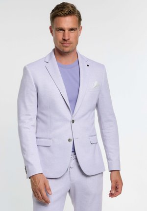 Blazer lavanda suave en tejido texturizado, con dos bolsillos delanteros, cierre de un botón y un pañuelo blanco en el bolsillo. Lleva puesto un top a juego.