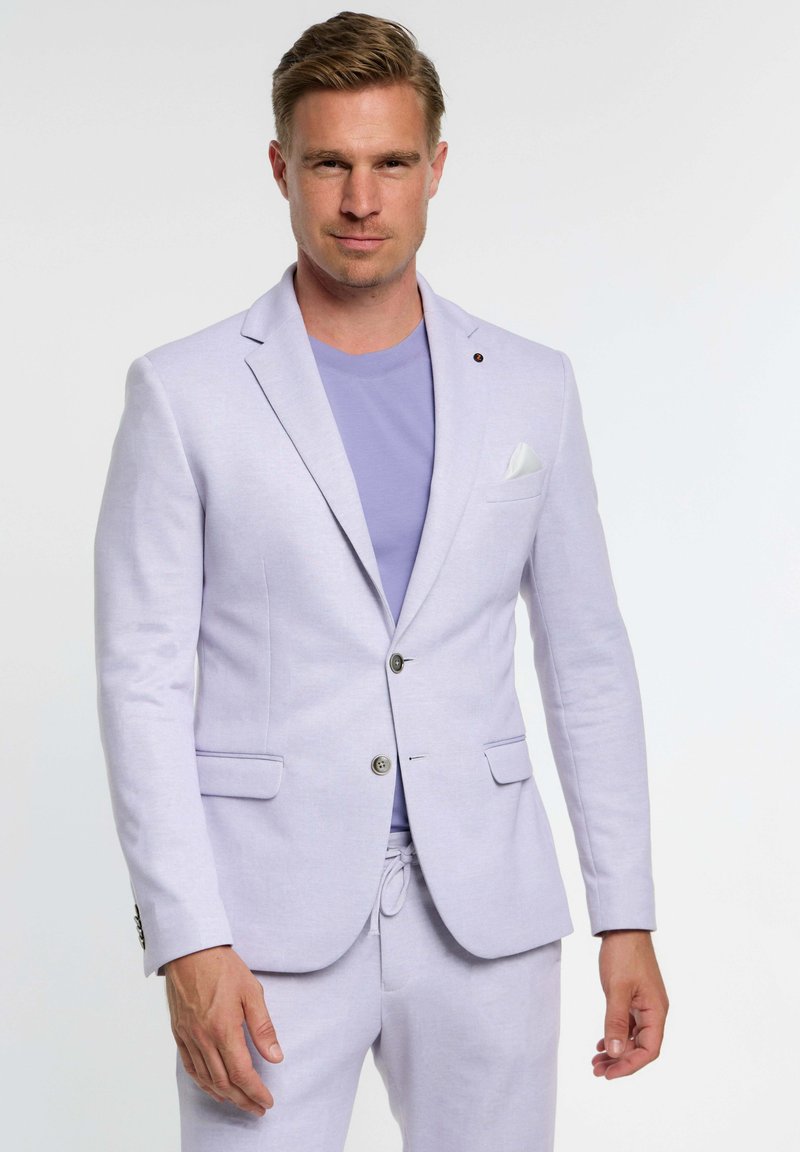 Blazer lavanda suave en tejido texturizado, con dos bolsillos delanteros, cierre de un botón y un pañuelo blanco en el bolsillo. Lleva puesto un top a juego.