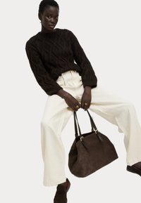 Maglione a maglia cable in marrone scuro, pantaloni a gamba larga color crema, borsa in suede marrone con manici in pelle e mocassini abbinati. Design semplice e textured.