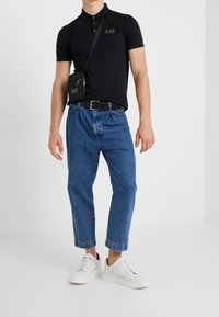 Svart polo skjorta med logotyp, blåjeans, vita sneakers och en liten svart axelväska. Avslappnad passform med en luftig silhuett.