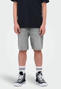 Shorts en denim gris avec une coupe droite, ourlet retroussé, portés avec des baskets montantes noires et des chaussettes blanches avec des rayures noires.