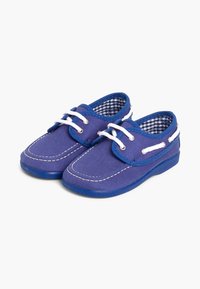 Zapatillas de lona azules con cordones blancos, punta redonda, costuras blancas en contraste y forro de tela de cuadros. Suela de goma plana para mayor durabilidad.
