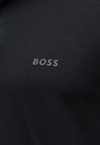 Tissu noir avec un texte gris en relief "BOSS" centré sur la surface, ressemblant à une étiquette ou un logo de vêtement.