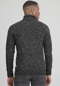 Texturiertes grau-schwarzes Strickpullover mit hohem Kragen, enganliegendem Design und Taillenbund. Besitzt subtile tonale Variationen im gesamten Stoff.