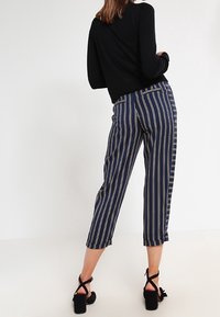 Marinblå och krämfärgade randiga byxor med en kortad design, som har en avslappnad passform och sidofickor, i kombination med svarta klacksandaler.
