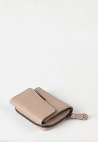 Portafoglio in pelle beige compatto con chiusura a zip e pattina con bottone, posizionato su una superficie bianca.