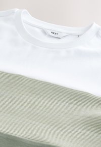 Rövid ujjú póló, fehér felső résszel és bordázott olívazöld alsó résszel, kerek nyakkivágással és puha pamut anyagból.