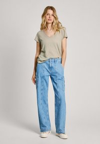 Camiseta verde claro con cuello en V combinada con pantalones cargo de mezclilla azul de cintura alta y pernera amplia, que cuentan con bolsillos laterales y un ajuste holgado.