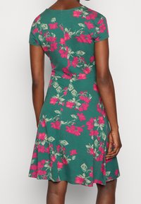 Grön blommig klänning, korta ärmar, figurnära byst, utsvängd kjol, livliga rosa blommor, bladvörter, texturerad tyg, knälång design.