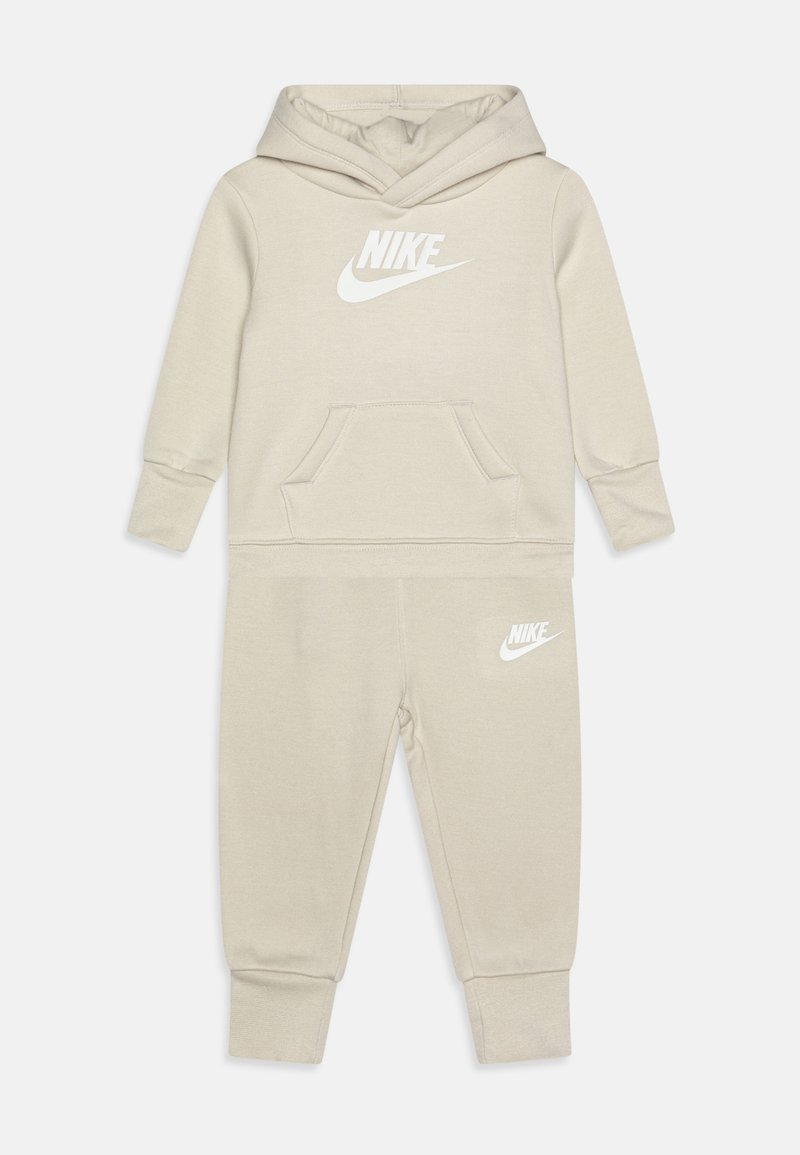 Conjunto de hoodie e calças Nike bege, com um bolso canguru à frente, punhos canelados e detalhes em branco no logótipo. Textura de tecido suave em todo o conjunto.