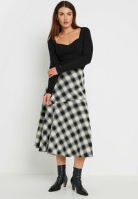 Un sweater noir à côtes avec un décolleté carré associé à une jupe midi à carreaux noir et blanc. Des bottines noires viennent parfaire la tenue.