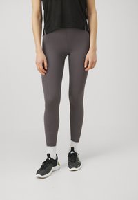 Sive, slim-fit legice iz raztegljivega materiala, z gladko teksturo in stranskimi žepi. V kombinaciji s črnimi športnimi čevlji in belimi nogavicami.