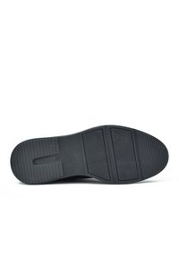 Suela de zapato de goma negra con secciones texturizadas y un patrón de agarre. La forma es plana con una punta redondeada y líneas de banda de rodadura distintas.