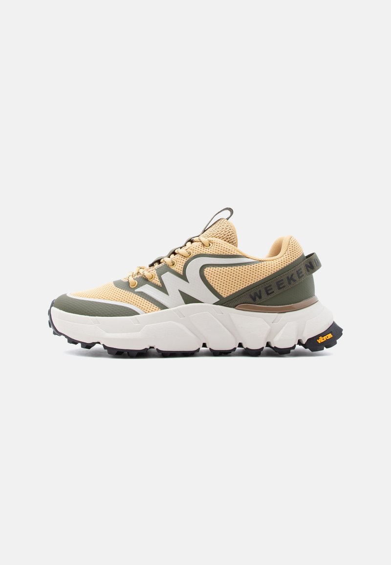 Baskets athlétiques beige et vert olive avec une semelle épaisse blanche, une accroche noire Vibram, une tige en mesh et le texte « WEEKEND » sur la sangle du talon.
