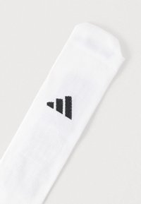 Λευκή αθλητική κάλτσα με ραβδωτή υφή, που φέρει μαύρο λογότυπο με τρεις διαγώνιες ρίγες. Στρογγυλή μύτη και ελαστική μανσέτα.