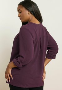 Långärmad skjorta i djup lila, med avslappnad passform, uppvikta ärmar med knappar och en ryggdetalj. Slät, strukturerad tyg.